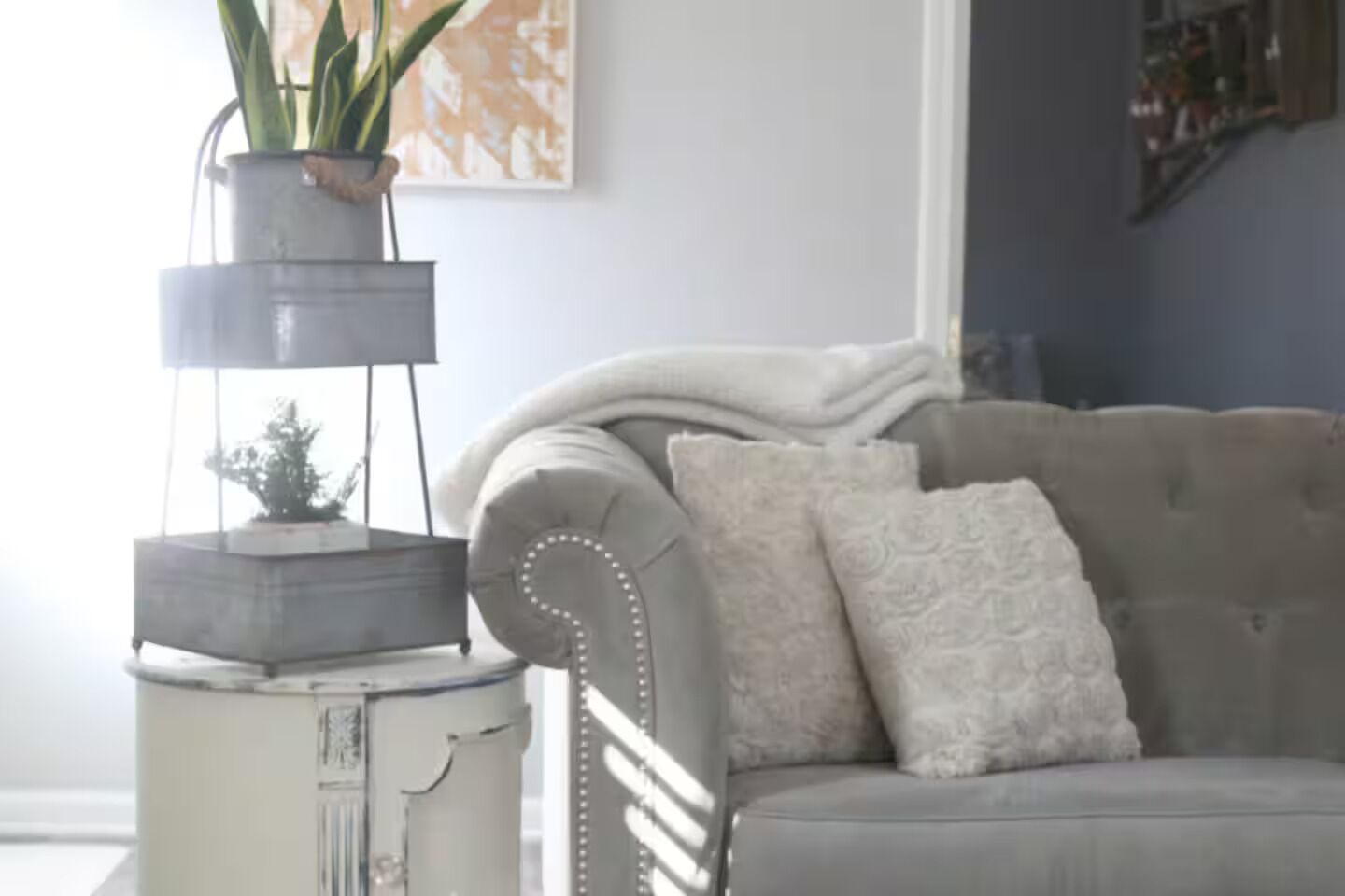 Un soggiorno con un divano grigio, cuscini decorativi, una pianta in vaso e un originale vaso a più livelli.