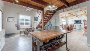 Una cocina amplia con una isla de madera, un comedor con sillas, una escalera y un televisor en la sala de estar.