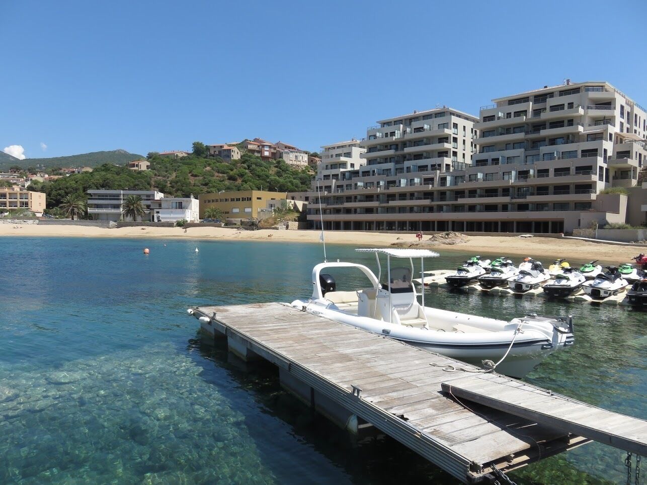 Un puerto deportivo con barcos amarrados, un muelle de madera y edificios al fondo.