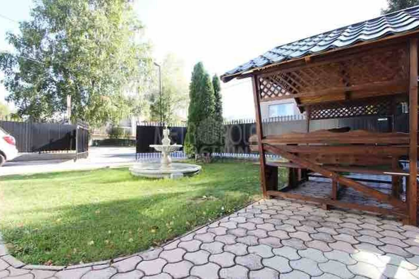 Un'area salotto esterna coperta con una pergola in legno, una fontana e un vialetto lastricato.