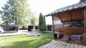 A covered outdoor seating area with a wooden pergola, a fountain, and a paved walkway. - Apartment Azi, Pejton Ilidža Apartments, Sarajevo (Pejton)