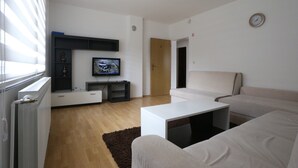 A modern living room with a flat-screen TV, a white sofa, a coffee table, and a wooden floor. - Apartment Azi, Pejton Ilidža Apartments, Sarajevo (Pejton)