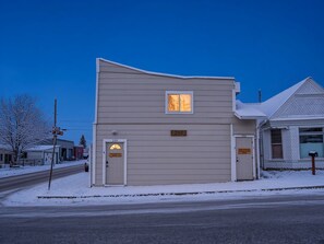 A two-story building with a flat roof, a small window, and a door with a number plate.