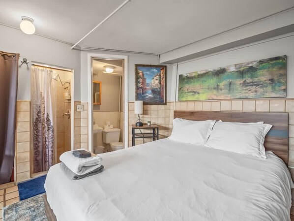 A hotel room with a bed, a painting, a bathroom, and a shower area.