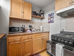 A kitchen with wooden cabinets, a microwave, a stove, and a coffee maker on a shelf.