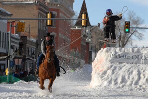 A horse and rider in motion, a person on skis, and a snow-covered area with a sign.