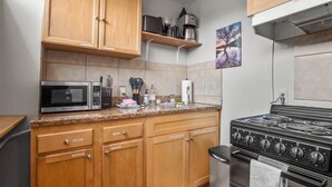 A kitchen with wooden cabinets, a microwave, a stove, and a coffee maker on a shelf. - 1BR Cozy Downtown Studio Condo: Hiking Nearby (Leadville)