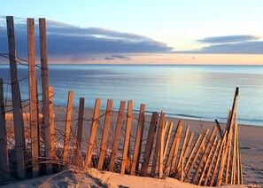 A wooden fence with barbed wire, leading to a beach with calm water and a clear sky. - Top Mast Resort- Shore House! Beach, Pool, Housekeeping and more!  (North Truro)