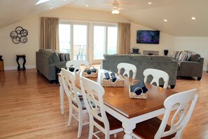 A spacious living area with a wooden dining table, white chairs, and a grey sofa. - Top Mast Resort- Shore House! Beach, Pool, Housekeeping and more!  (North Truro)