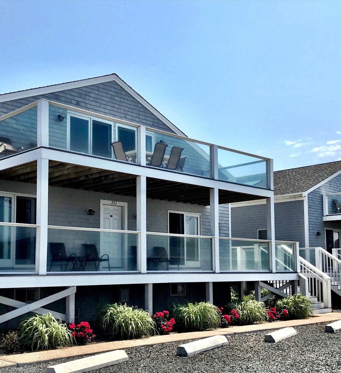 A modern two-story house with a balcony, large windows, and a gravel driveway.