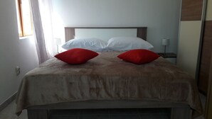 A hotel room with a bed, two red pillows, white pillows, a wooden headboard, and a nightstand with a lamp.