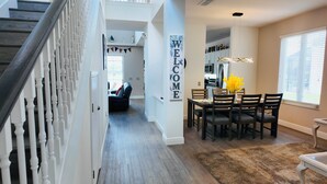 A modern interior with a staircase, a dining area with a 'WELCOME' sign, and a kitchen in the background. - 4 Bed, 3.5 Bath, 2 Masters Large 30’ South Facing Pool / 8’ Kiddie Pool Lakeside (Kissimmee)