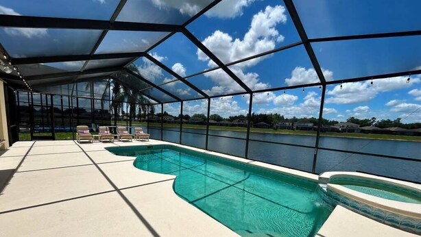 A covered outdoor swimming pool with a view of a lake and houses in the background. - 4 Bed, 3.5 Bath, 2 Masters Large 30’ South Facing Pool / 8’ Kiddie Pool Lakeside (Kissimmee)