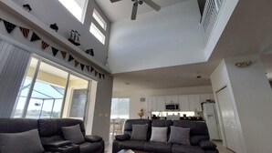 A spacious living room with two black sofas, a ceiling fan, and a kitchen area with white cabinets. - 4 Bed, 3.5 Bath, 2 Masters Large 30’ South Facing Pool / 8’ Kiddie Pool Lakeside (Kissimmee)