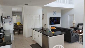 A modern kitchen with a central island, a dining area with a table and chairs, a living room with a sofa and a TV, and a balcony with a railing. - 4 Bed, 3.5 Bath, 2 Masters Large 30’ South Facing Pool / 8’ Kiddie Pool Lakeside (Kissimmee)