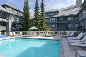 A pool area with lounge chairs and a lifebuoy, surrounded by buildings with balconies and large windows.