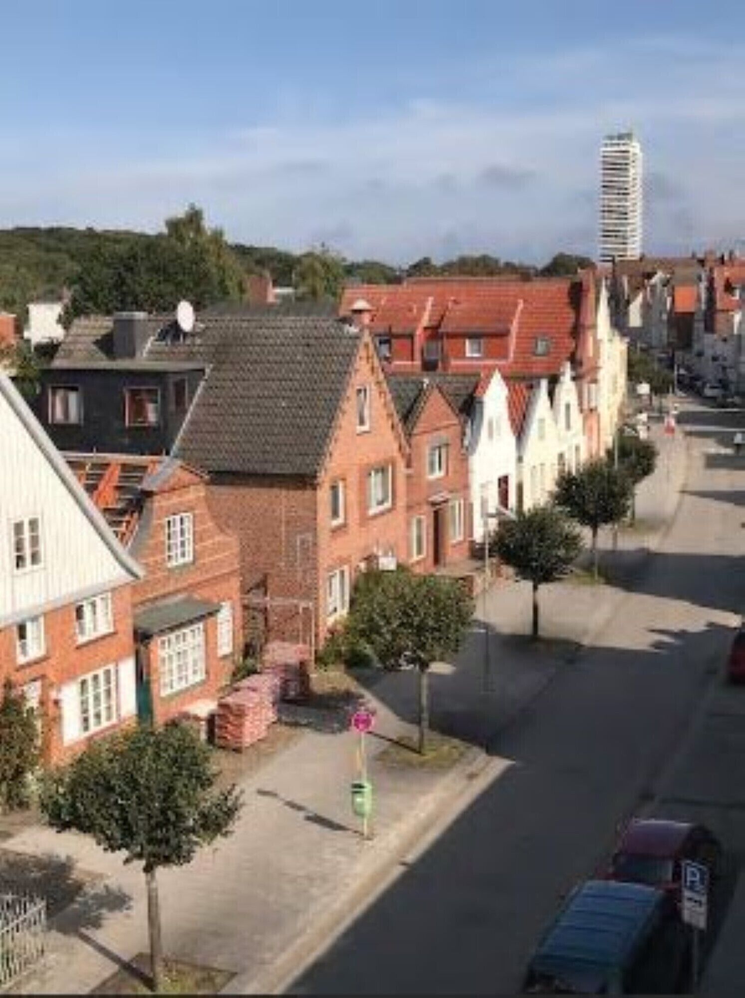 A street view of a residential area with traditional European-style houses, a clear sky, and a parked car.