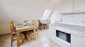 Une cuisine moderne avec des armoires blanches, un four encastré et un coin repas comprenant une table et des chaises en bois.