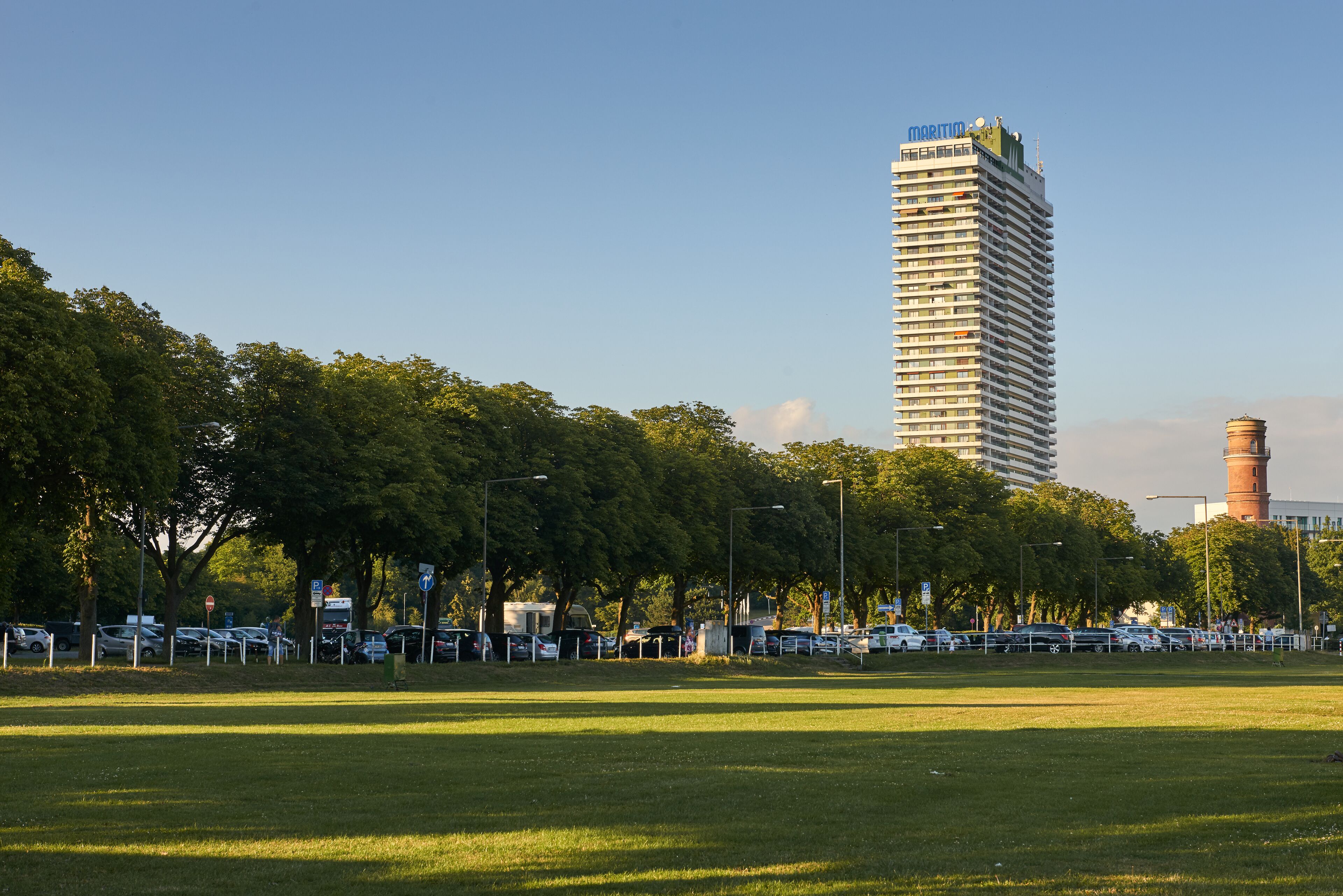 A tall hotel with a modern design, surrounded by a grassy area and trees.
