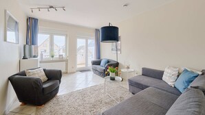Un salon moderne avec deux canapés gris, un fauteuil noir, une table basse blanche et une suspension bleue.
