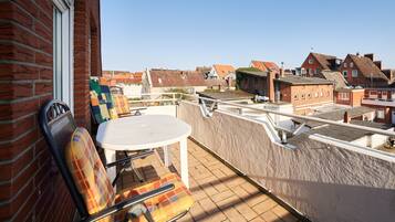A balcony with a table and chairs, overlooking a residential area with brick houses.