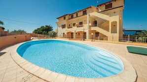 A swimming pool with a tiled deck, a multi-story building with balconies, and a clear blue sky. - Awesome apartment in Castelsardo SS with outdoor swimming pool (Castelsardo SS)