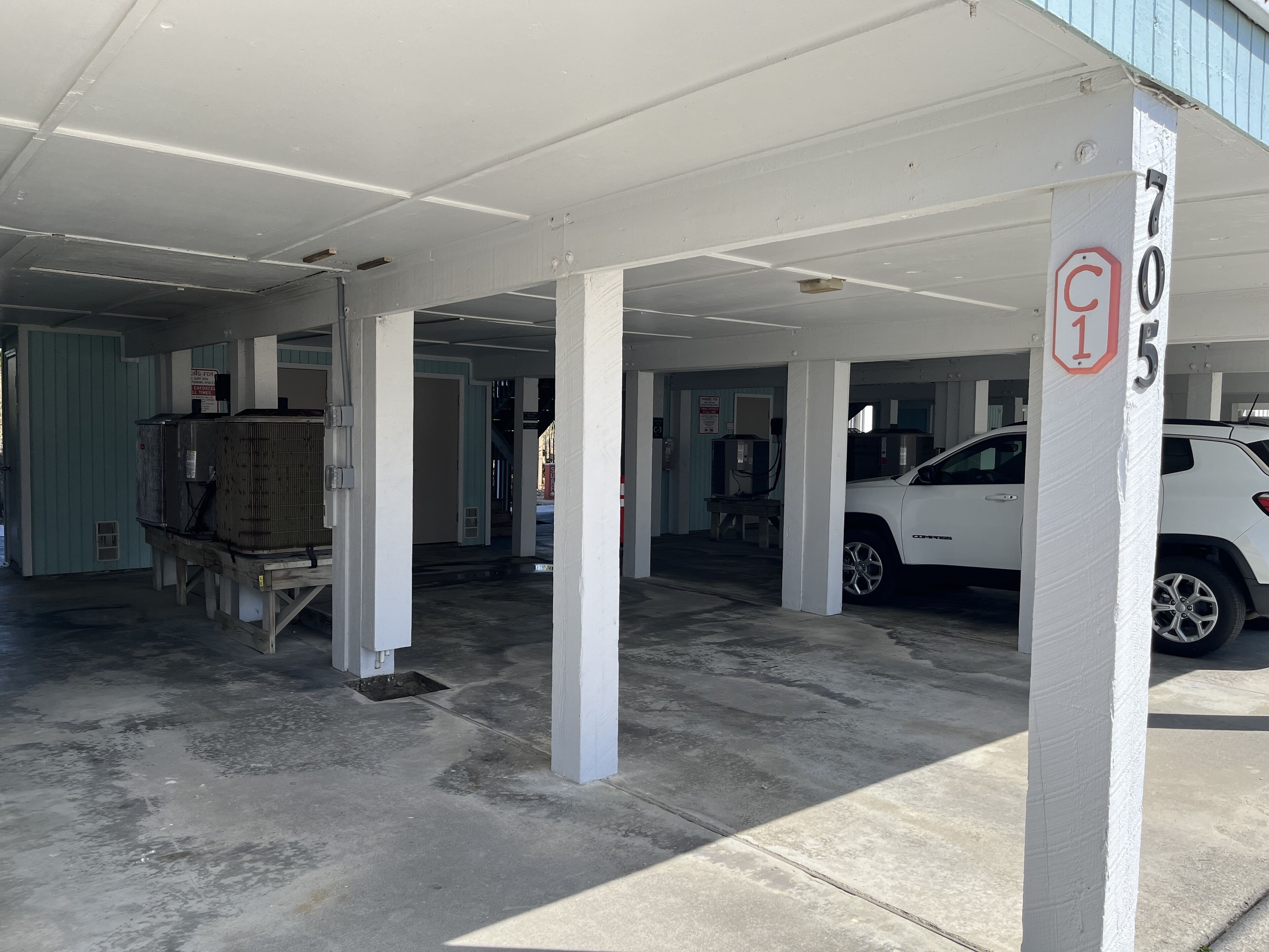 A parking garage with white pillars, a white car, and a sign with the number 705.