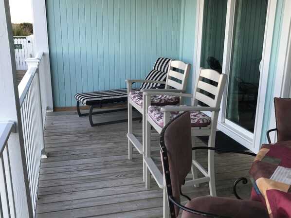 A wooden deck with two lounge chairs and a bench, a white railing, and a door with a 'Not a Public Access' sign.