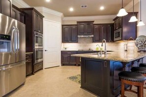 Une cuisine moderne avec des meubles de couleur sombre, des appareils en acier inoxydable, un îlot central et des luminaires suspendus.