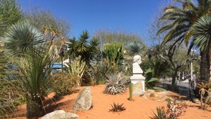 Ein Garten mit verschiedenen Kakteen, Pflanzen, einer Statue und einem gepflasterten Weg.