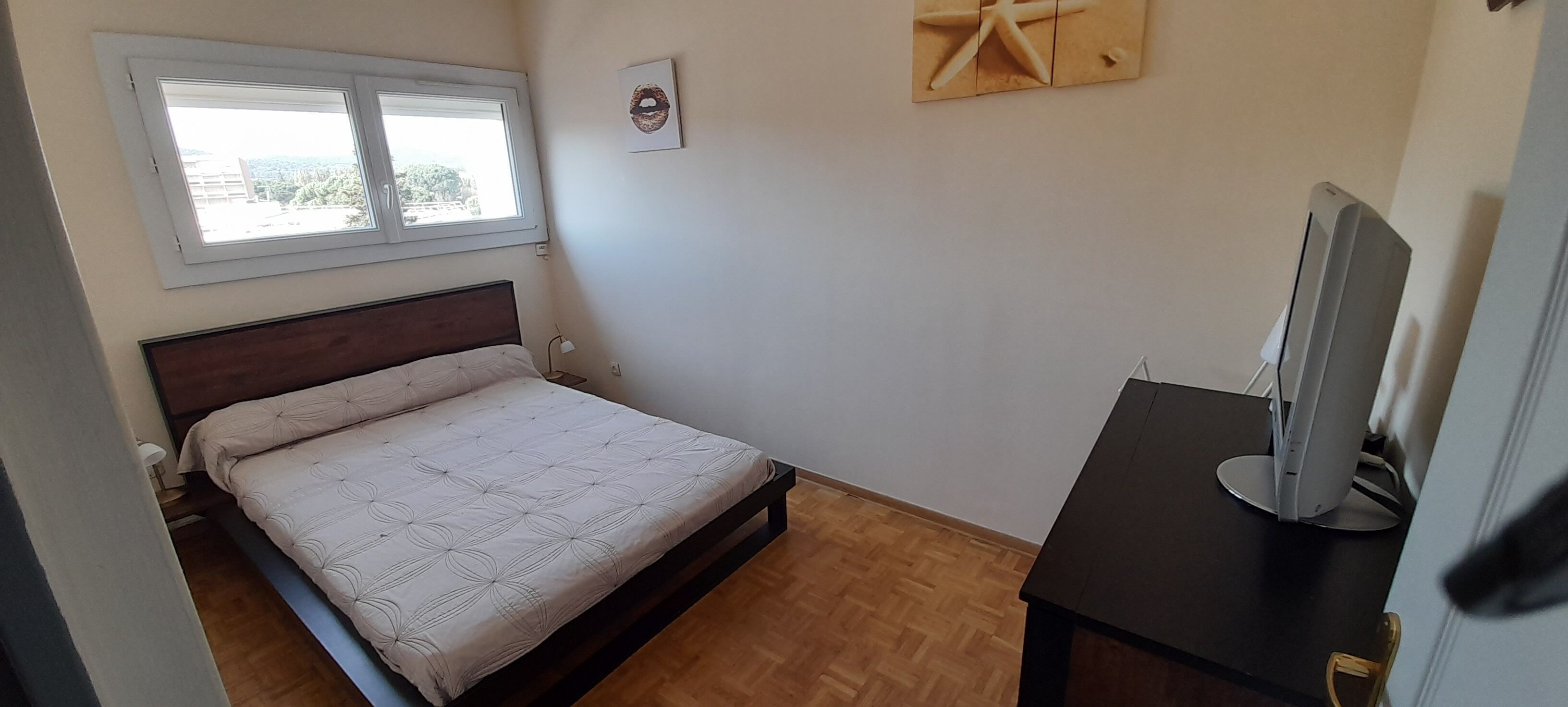 A bedroom with a bed, a desk, a computer, a window, and a wall decoration.