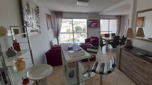 Ein modernes Hotelzimmer mit Essbereich, einer Couch, einem Schreibtisch mit Computer und Blick auf die Stadt durch große Fenster.