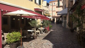 Eine Kopfsteinpflasterstraße mit Außenbestuhlung und Sonnenschirmen, die eine Café- oder Restaurantatmosphäre vermittelt.
