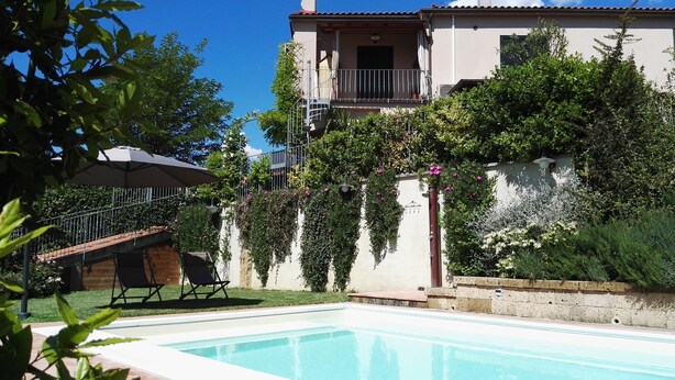 Un espace aménagé au bord d’une piscine à l’eau d’un bleu limpide, avec une terrasse en bois et un bâtiment doté d’un balcon.