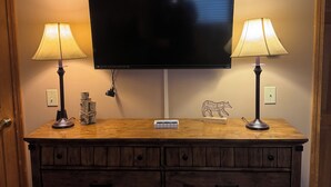 Um suporte de TV de madeira com uma televisão de tela plana, duas luminárias e um quadro emoldurado acima da TV.