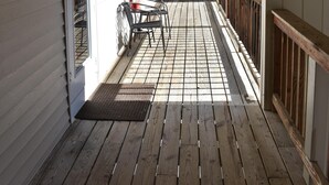 Um deck de madeira com guarda-corpo, uma porta e uma cadeira.
