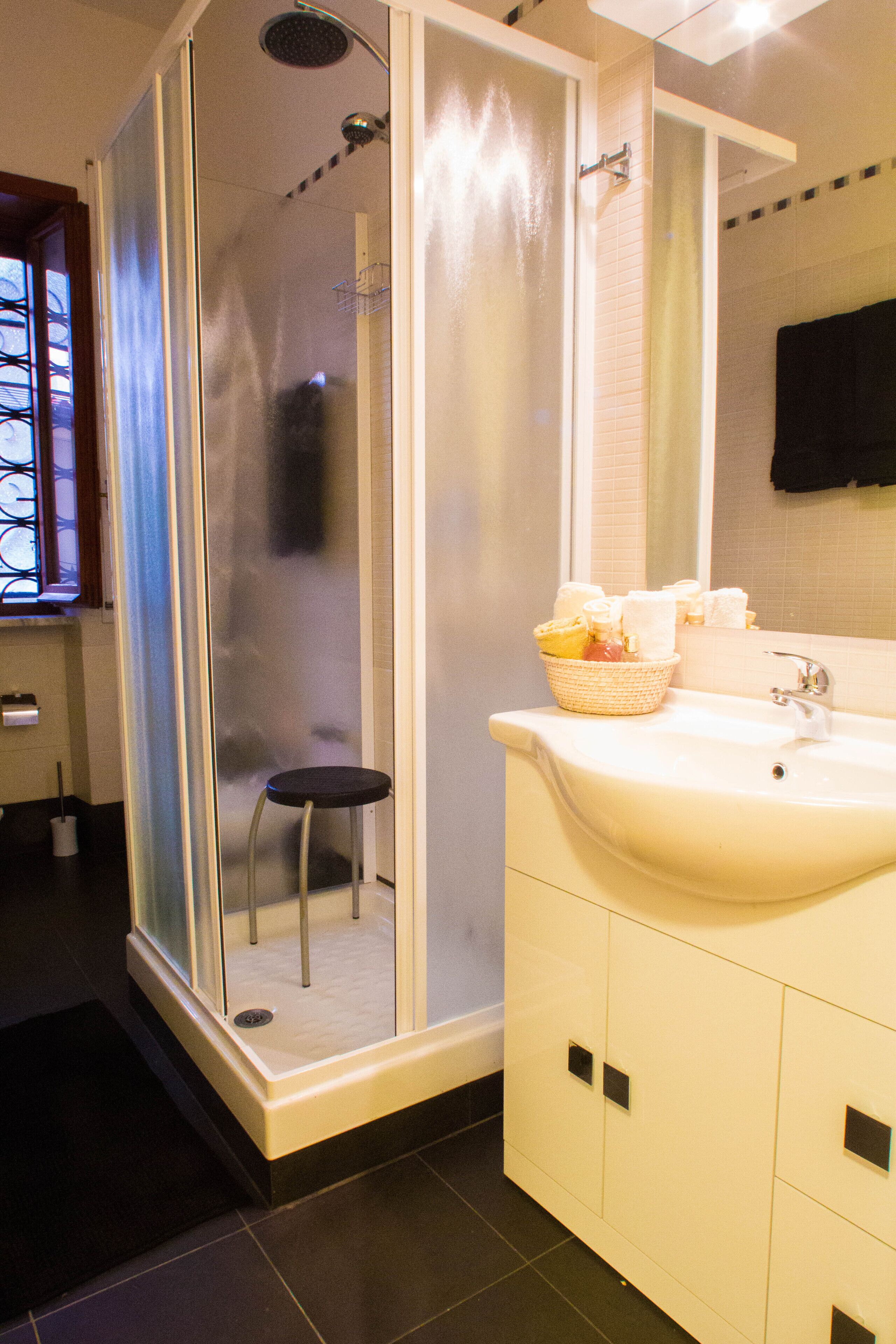 A bathroom with a glass-enclosed shower, a sink with a basket of toiletries, and a mirror above the sink.