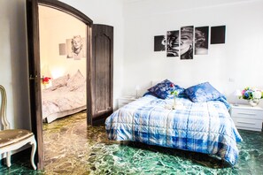 Un dormitorio con cama, una silla, una mesita de noche y una pared decorada con marcos.