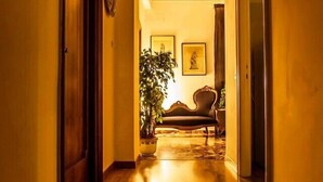 A hallway with a wooden floor, a potted plant, and a sofa in the background.