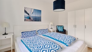 Une chambre à coucher comprenant un lit, une table de chevet, une lampe, une armoire et un tableau représentant un voilier.
