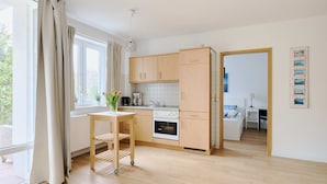 Une cuisine moderne avec des meubles en bois, un plan de travail blanc et une petite table agrémentée d’un vase de fleurs.