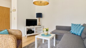 Un salon moderne avec un téléviseur, un canapé et une petite table sur laquelle est posé un vase de fleurs.