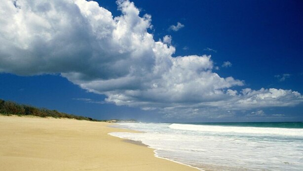 Una playa con una amplia orilla arenosa y olas suaves.