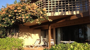 Un hotel con un área de estar cubierta al aire libre, un balcón con celosía y abundante vegetación.
