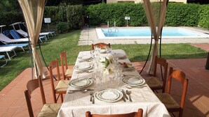 Un espace extérieur aménagé pour les repas, avec une table dressée pour quatre personnes, entourée de chaises, et une piscine en arrière-plan.