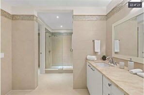 Een moderne badkamer met een ruime douche, een grote spiegel en een wastafel met aanrecht.