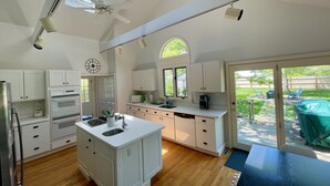 A spacious kitchen with a central island, built-in oven, and a large window overlooking a backyard. - Beautiful Home with Central A/C. Walk to the Beach, Large Yard (Dennis Port)