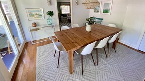 A dining area with a wooden table, white chairs, a patterned rug, and a hanging light fixture. - Beautiful Home with Central A/C. Walk to the Beach, Large Yard (Dennis Port)