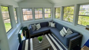 A sunroom with a dark blue sofa, a striped rug, and a potted plant. - Beautiful Home with Central A/C. Walk to the Beach, Large Yard (Dennis Port)