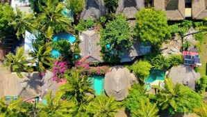 Eine Vogelperspektive zeigt einen luxuriösen Urlaubsort mit mehreren Schwimmbecken, üppiger Vegetation und großen Felsformationen.